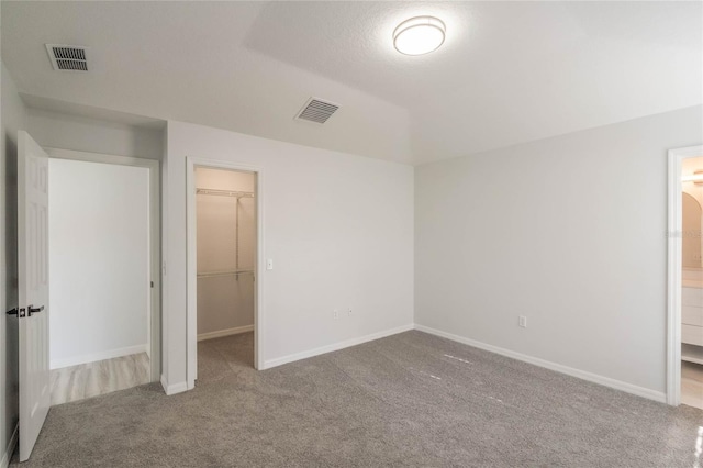 unfurnished bedroom featuring a closet, a spacious closet, ensuite bathroom, and carpet flooring