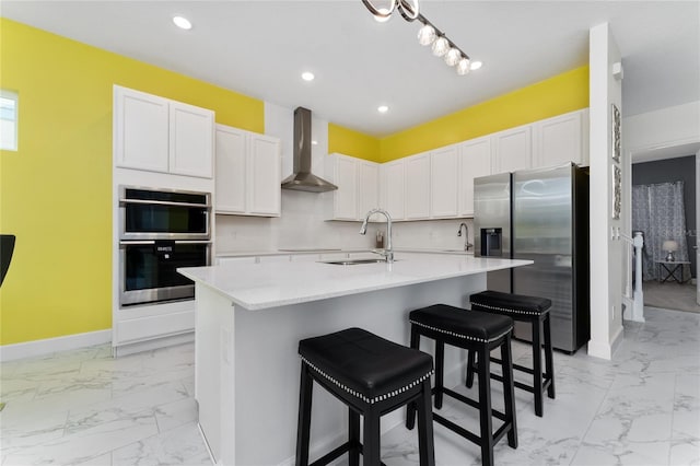 kitchen with sink, appliances with stainless steel finishes, a kitchen breakfast bar, an island with sink, and wall chimney exhaust hood