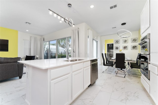 kitchen featuring white cabinetry, hanging light fixtures, sink, and an island with sink