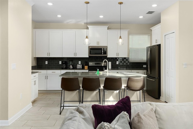 kitchen featuring sink, white cabinetry, decorative light fixtures, a center island with sink, and appliances with stainless steel finishes