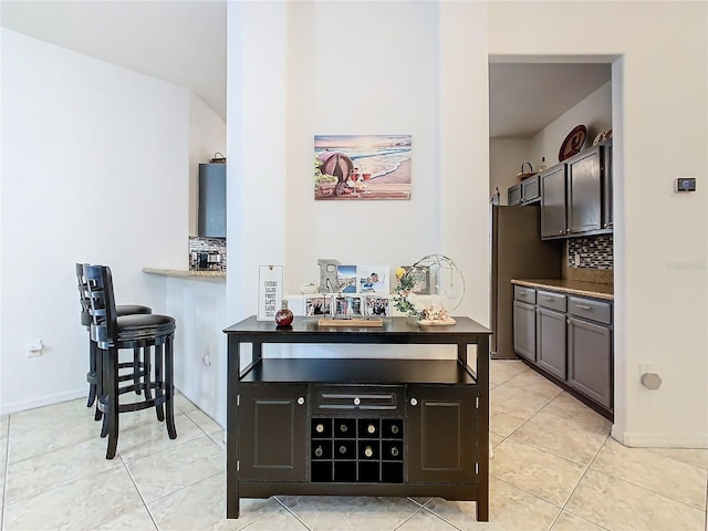 kitchen featuring dark brown cabinetry, light tile patterned floors, decorative backsplash, and stainless steel fridge