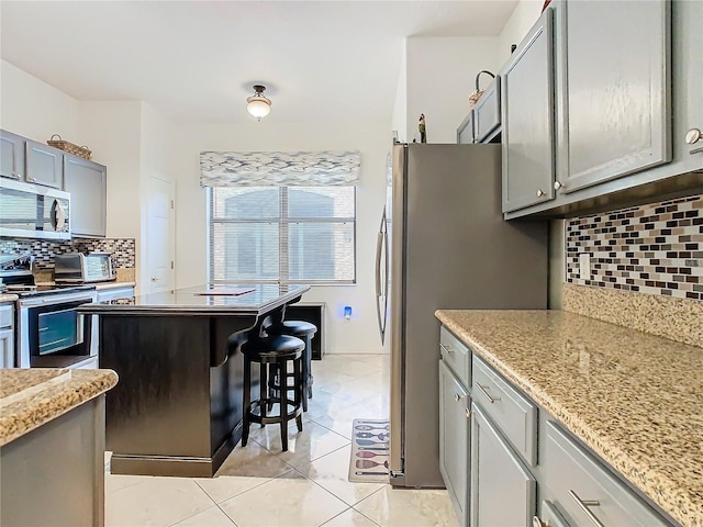 kitchen featuring appliances with stainless steel finishes, tasteful backsplash, gray cabinetry, light tile patterned floors, and light stone countertops