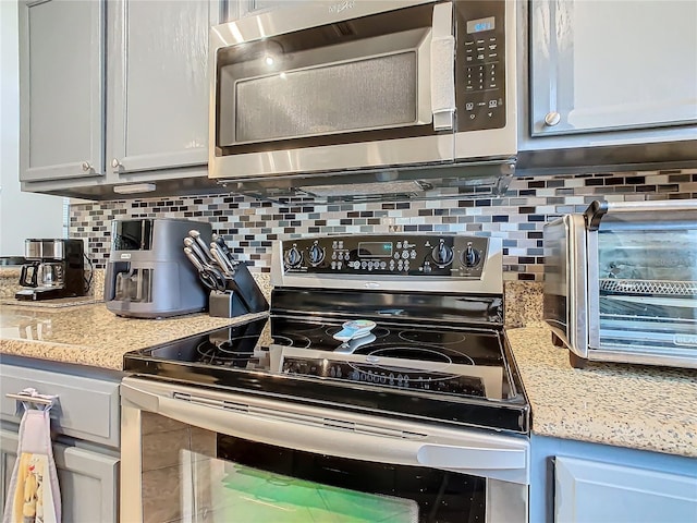 kitchen with light stone countertops, appliances with stainless steel finishes, and backsplash