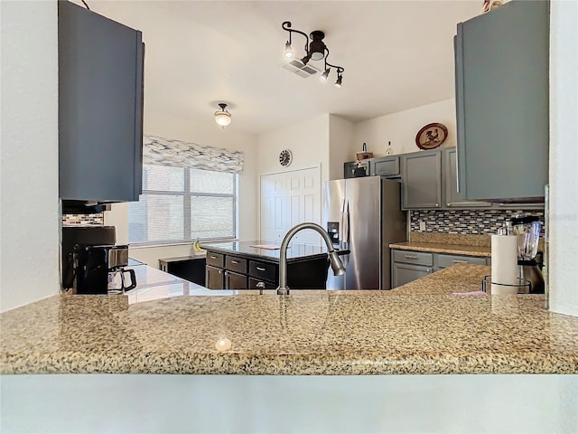 kitchen with light stone countertops, kitchen peninsula, stainless steel fridge, and decorative backsplash