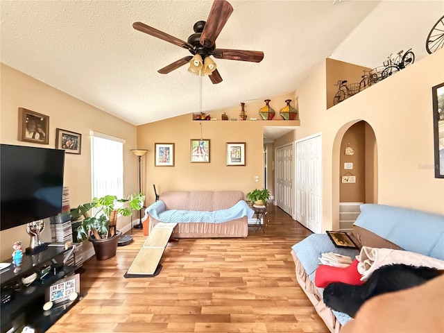 living room with ceiling fan, lofted ceiling, a textured ceiling, and light hardwood / wood-style floors