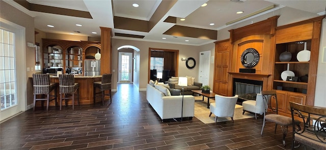 living room with coffered ceiling, crown molding, a large fireplace, and bar