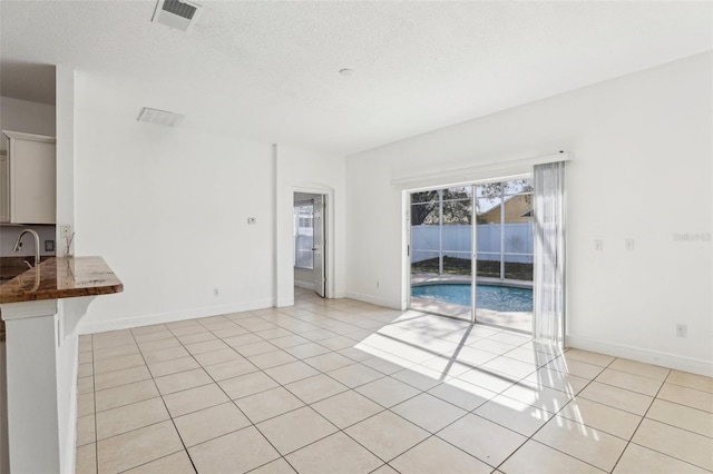 unfurnished living room with sink, a textured ceiling, and light tile patterned floors