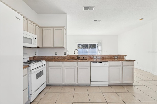 kitchen with sink, white appliances, a textured ceiling, light tile patterned flooring, and kitchen peninsula