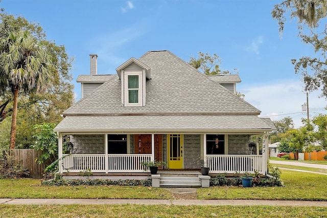 farmhouse-style home featuring a front lawn, fence, a porch, roof with shingles, and a chimney