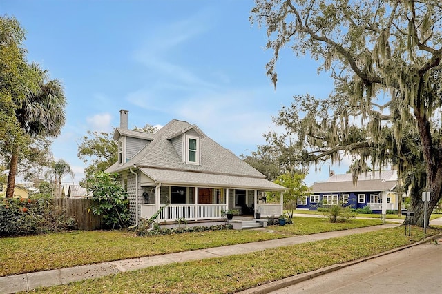 view of front of home with a porch, a shingled roof, a front lawn, and fence