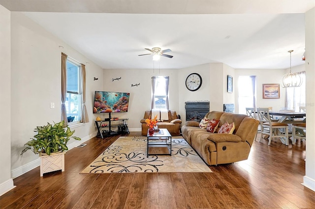 living room featuring ceiling fan with notable chandelier, a fireplace, baseboards, and wood finished floors