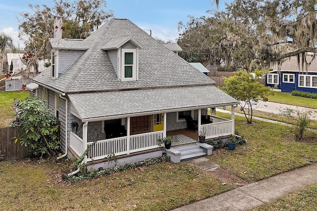 view of front of house featuring a porch, roof with shingles, a front yard, and fence