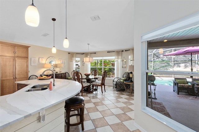 kitchen featuring a kitchen breakfast bar, decorative light fixtures, light stone countertops, and sink