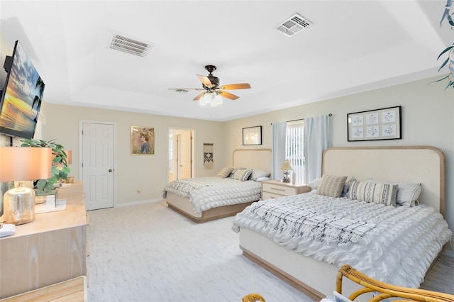 bedroom with a raised ceiling, light colored carpet, and ceiling fan