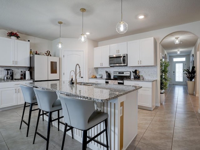 kitchen with appliances with stainless steel finishes, a kitchen island with sink, white cabinets, and decorative light fixtures