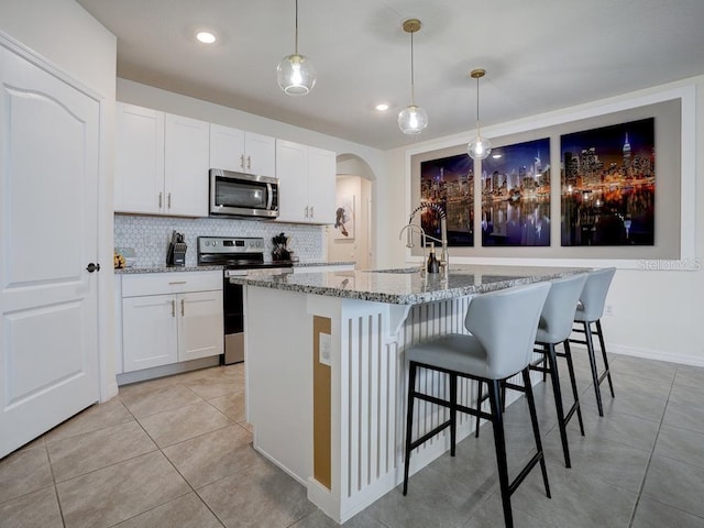 kitchen featuring white cabinetry, stainless steel appliances, light stone counters, a center island with sink, and decorative light fixtures