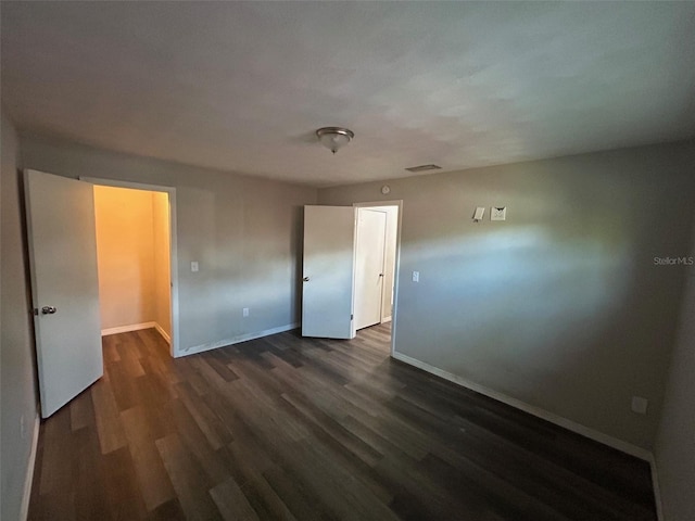 unfurnished bedroom with baseboards, dark wood-style floors, and visible vents