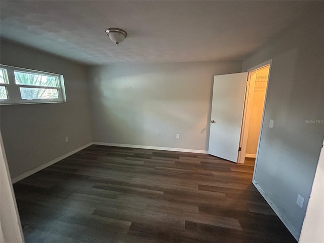 unfurnished room with dark wood-type flooring and baseboards