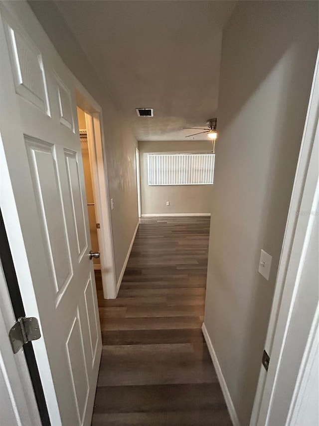 corridor featuring dark wood-style flooring, visible vents, and baseboards