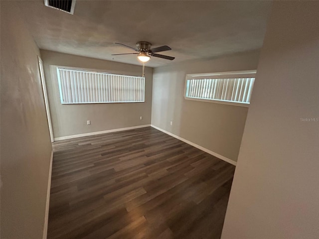 empty room featuring dark wood-style flooring, visible vents, ceiling fan, and baseboards