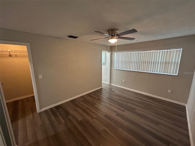 unfurnished bedroom featuring dark wood-type flooring, visible vents, a spacious closet, and baseboards