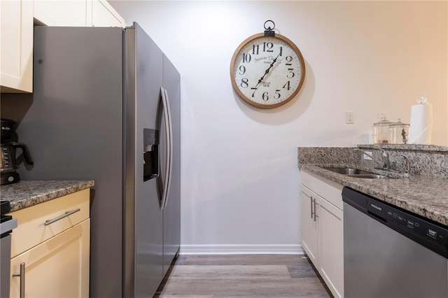 kitchen featuring sink, light wood-type flooring, dark stone countertops, appliances with stainless steel finishes, and white cabinets