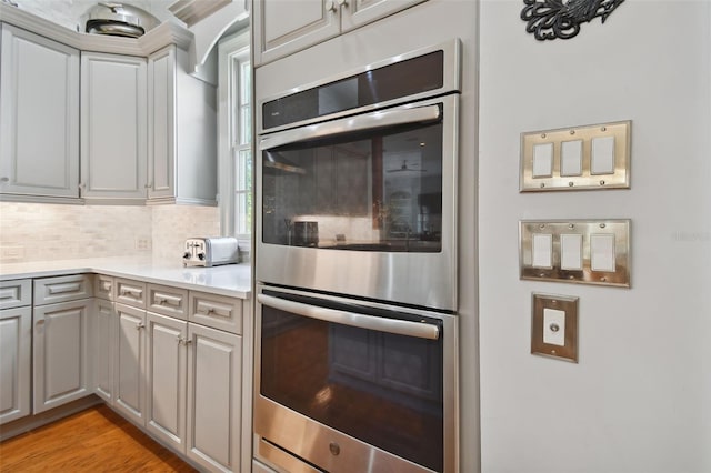 kitchen featuring gray cabinetry, double oven, backsplash, and light hardwood / wood-style floors