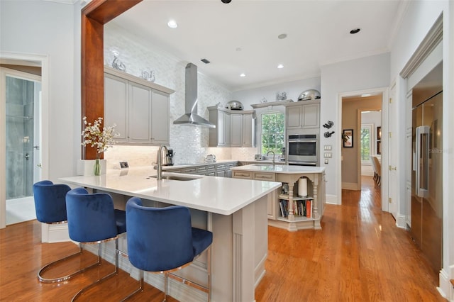 kitchen with sink, a kitchen breakfast bar, kitchen peninsula, oven, and wall chimney range hood