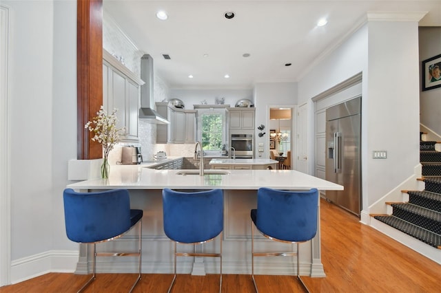 kitchen with sink, wall chimney range hood, a breakfast bar area, stainless steel appliances, and kitchen peninsula