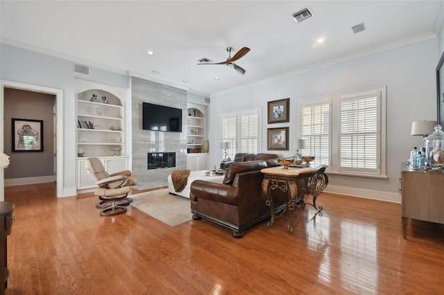 living room featuring built in shelves, a premium fireplace, crown molding, and hardwood / wood-style floors