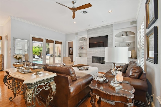 living room with wood-type flooring, ornamental molding, built in features, and a high end fireplace