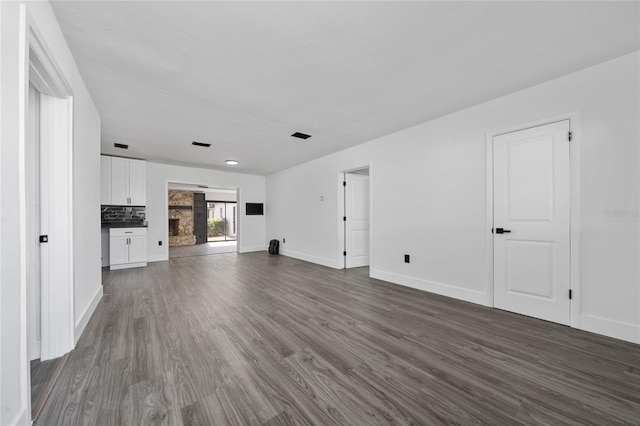 unfurnished living room with a stone fireplace and dark hardwood / wood-style flooring