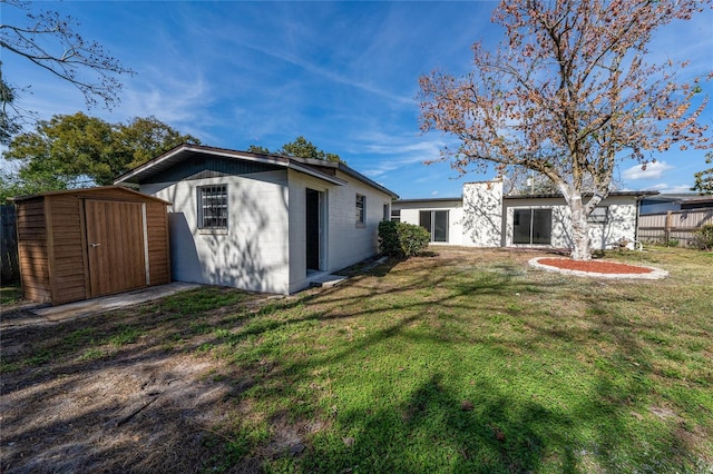 rear view of house with a storage shed, a lawn, concrete block siding, an outbuilding, and fence