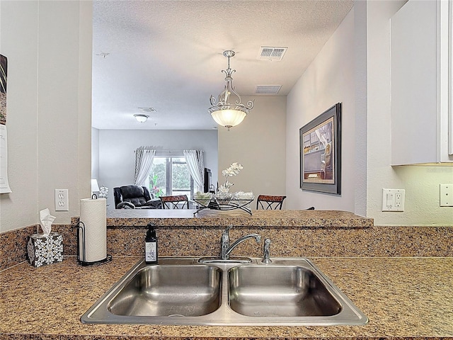 kitchen featuring a sink, a textured ceiling, hanging light fixtures, open floor plan, and visible vents