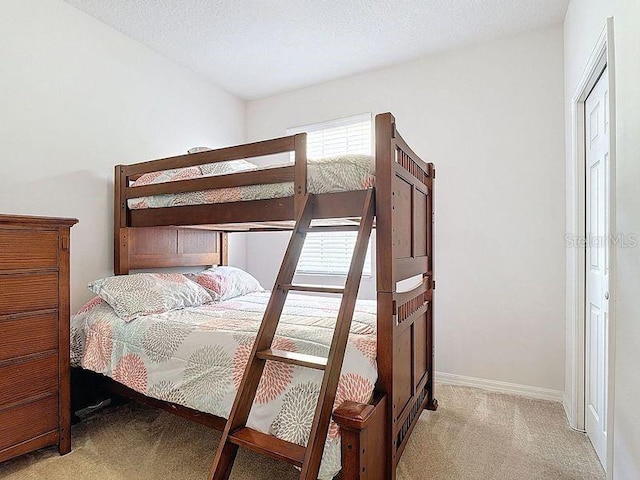 bedroom with baseboards, light colored carpet, and a textured ceiling