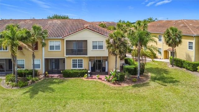 rear view of property with a tiled roof, stucco siding, and a lawn