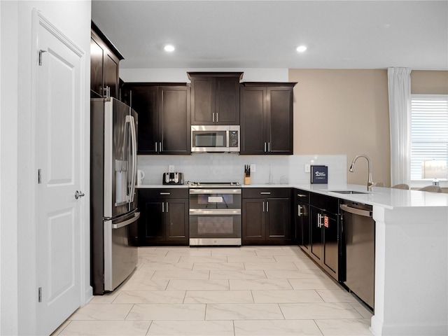 kitchen featuring tasteful backsplash, sink, dark brown cabinetry, kitchen peninsula, and stainless steel appliances