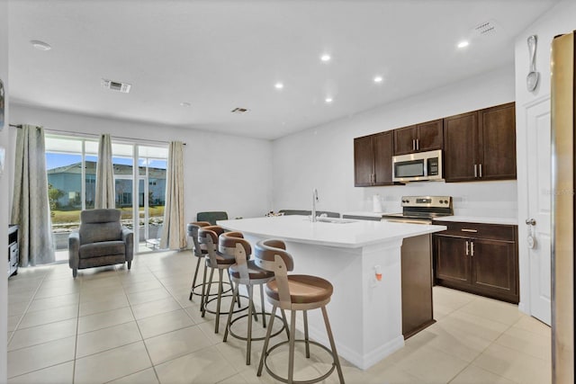 kitchen featuring appliances with stainless steel finishes, sink, a kitchen bar, light tile patterned floors, and a center island with sink