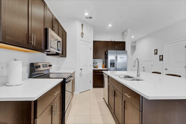 kitchen with an island with sink, stainless steel appliances, sink, and dark brown cabinets