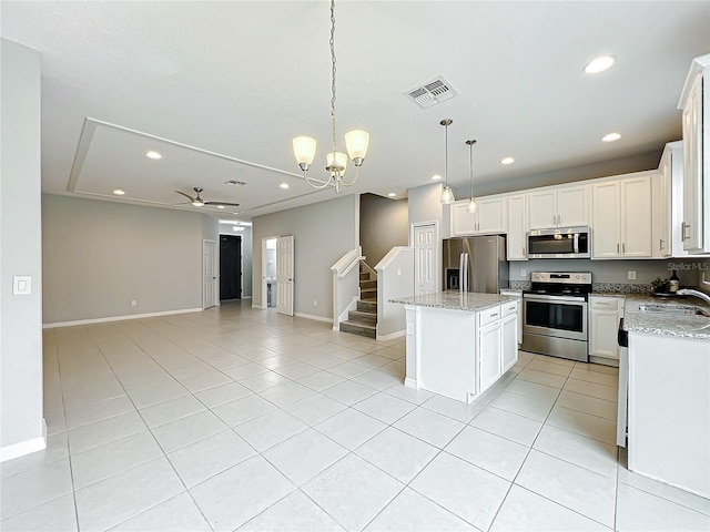 kitchen with stainless steel appliances, a kitchen island, visible vents, open floor plan, and light stone countertops