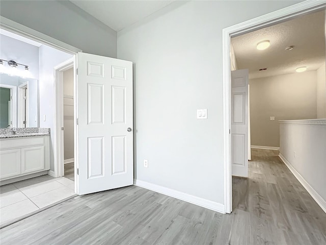 unfurnished bedroom featuring a sink, light wood-style flooring, baseboards, and ensuite bathroom