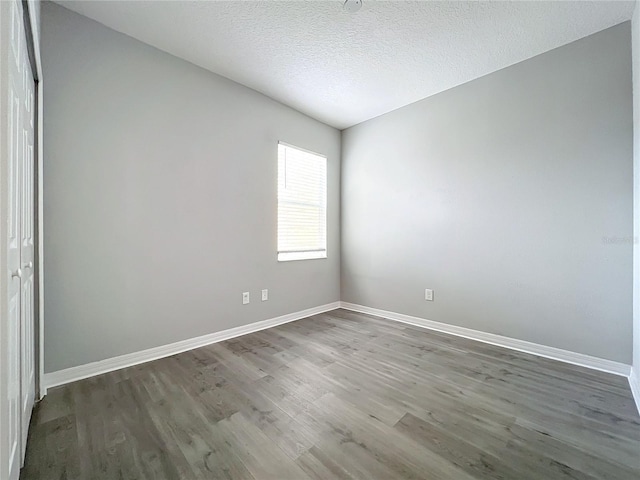 unfurnished room featuring a textured ceiling, baseboards, and wood finished floors