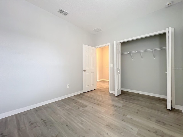 unfurnished bedroom featuring a closet, visible vents, baseboards, and wood finished floors