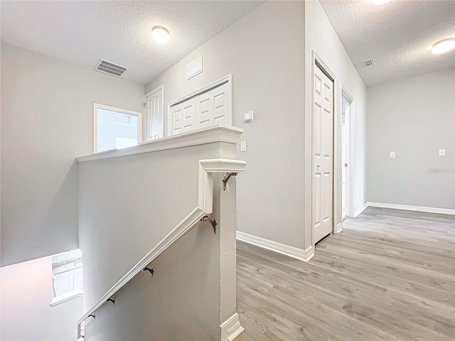 corridor featuring baseboards, visible vents, a textured ceiling, an upstairs landing, and light wood-type flooring