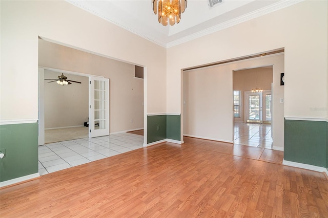 unfurnished room featuring french doors, light hardwood / wood-style flooring, ornamental molding, ceiling fan with notable chandelier, and a high ceiling