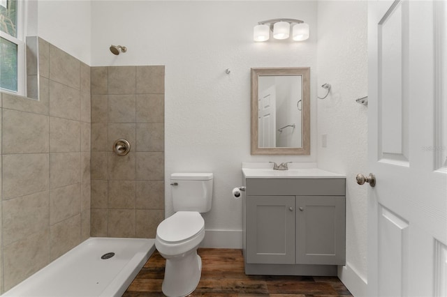 bathroom with a tile shower, vanity, wood-type flooring, and toilet