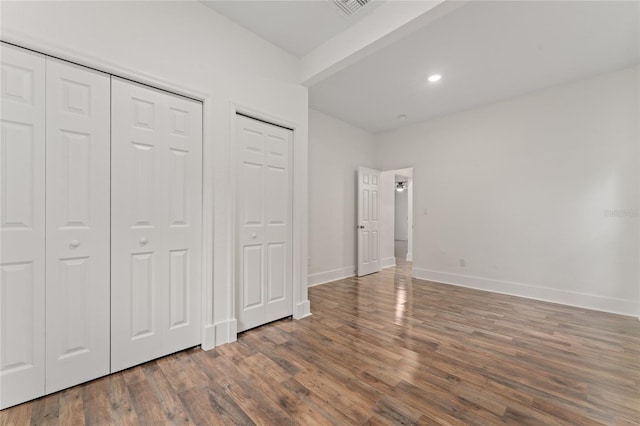 unfurnished bedroom featuring wood-type flooring and multiple closets