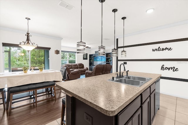 kitchen featuring tile patterned floors, sink, crown molding, hanging light fixtures, and an island with sink