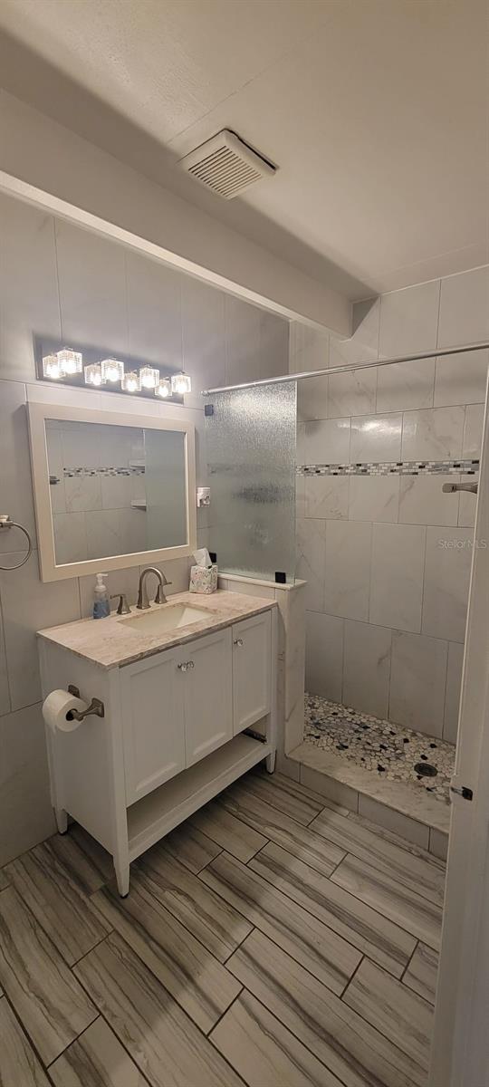 bathroom with a tile shower and vanity