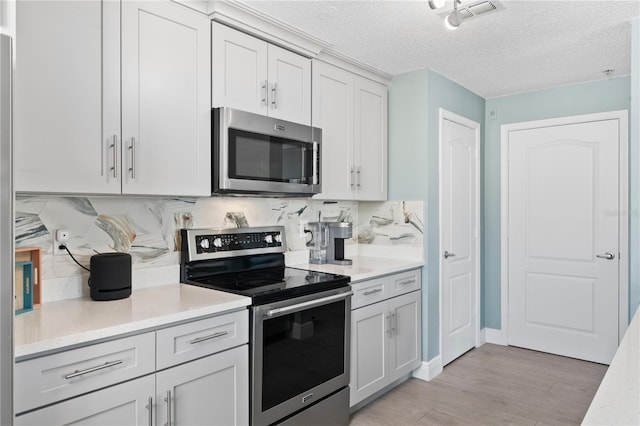 kitchen featuring decorative backsplash, light hardwood / wood-style flooring, a textured ceiling, and appliances with stainless steel finishes